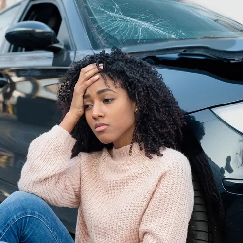Injured driver holds her head while leaning on her vehicle after a crash